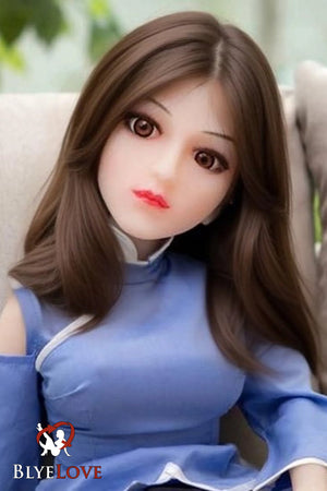 A realistic sex doll with brown hair and a blue outfit, sitting upright with a subtle smile.